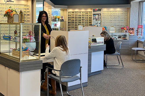 An optician s office with a woman standing behind the counter, assisting customers.
