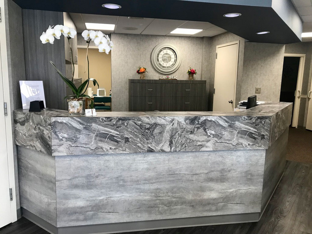 An image of a modern reception desk with a marble countertop and a wood floor, featuring a large floral arrangement in the background.