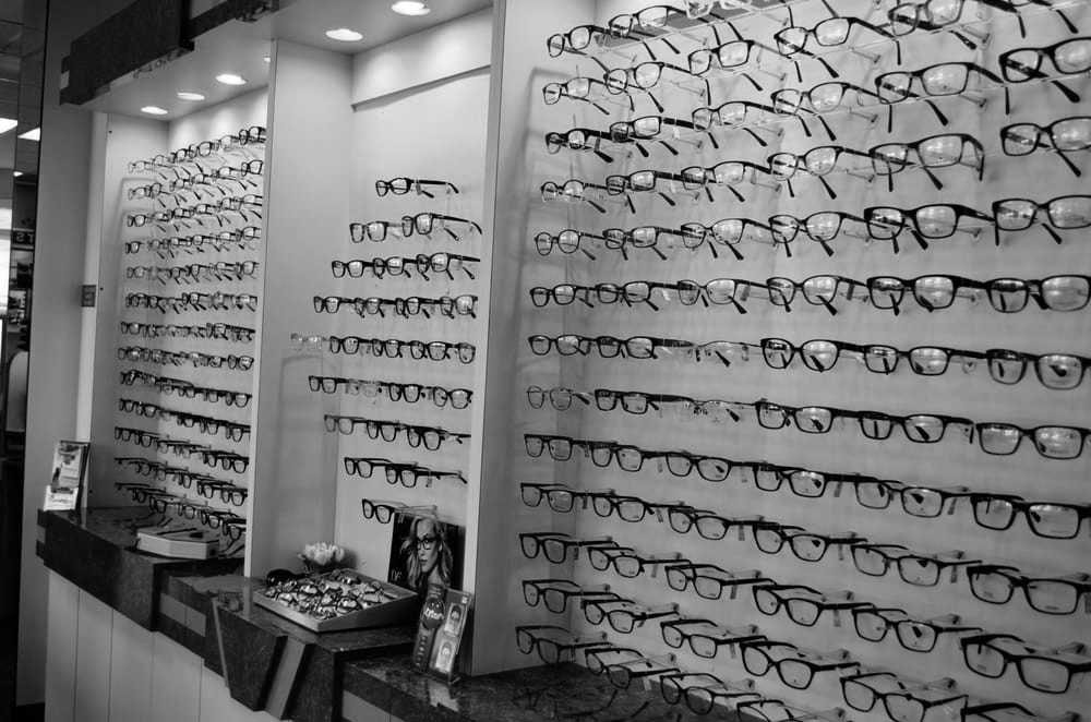 The image displays a large collection of eyeglasses on display in what appears to be an optical store, with various styles and frames visible.