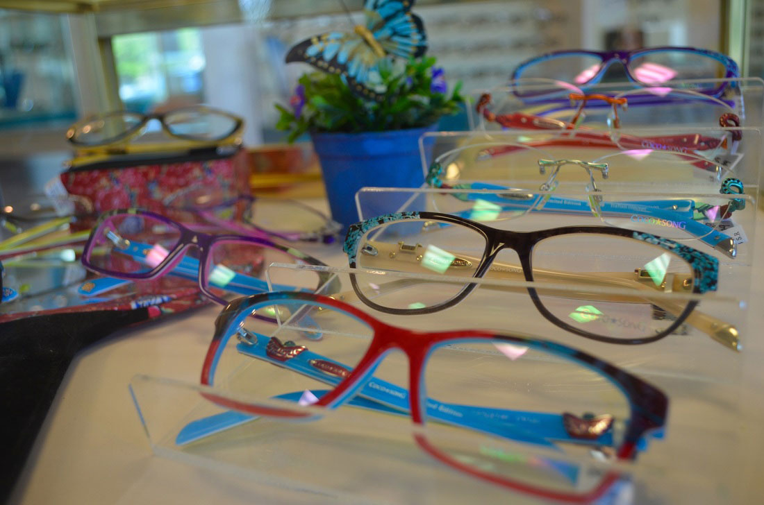 The image shows a display of colorful eyeglass frames with various designs and colors, including red, blue, purple, and black.