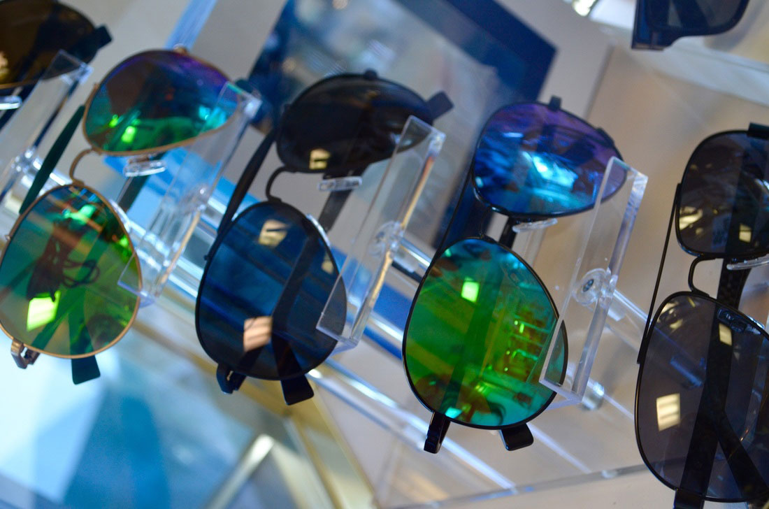 The image displays a collection of sunglasses with various colored frames and lenses, showcased in a display case.