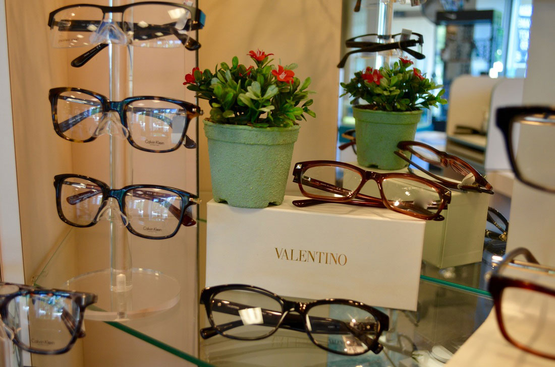 Eyeglasses on display in a store, with a potted plant and a sign with the name  Valentino .