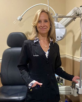 Woman standing in front of a dental chair, wearing medical scrubs and holding a stethoscope.
