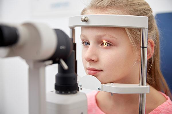 A young girl is seated in front of an eye examination machine, looking intently through the device.