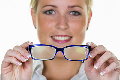 A woman holding a pair of blue glasses, smiling at the camera.