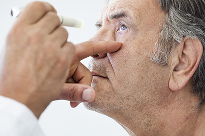 The image shows a medical professional, likely an optometrist or ophthalmologist, performing an eye examination on a patient.