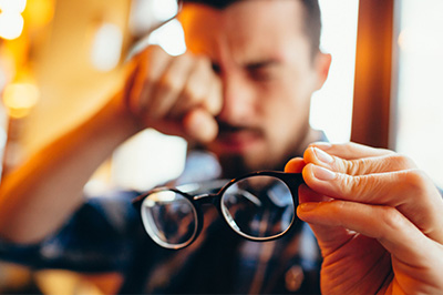 A man wearing glasses is holding them up to his face, looking down with a serious expression.