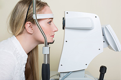 A woman is looking through an eye machine, likely for a vision test.