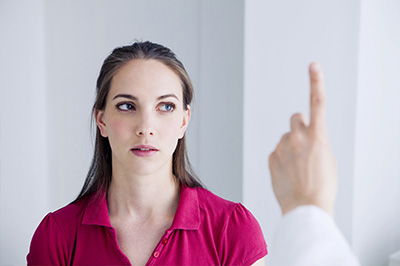 A woman in a red shirt looking up at a man s hand pointing to her face.