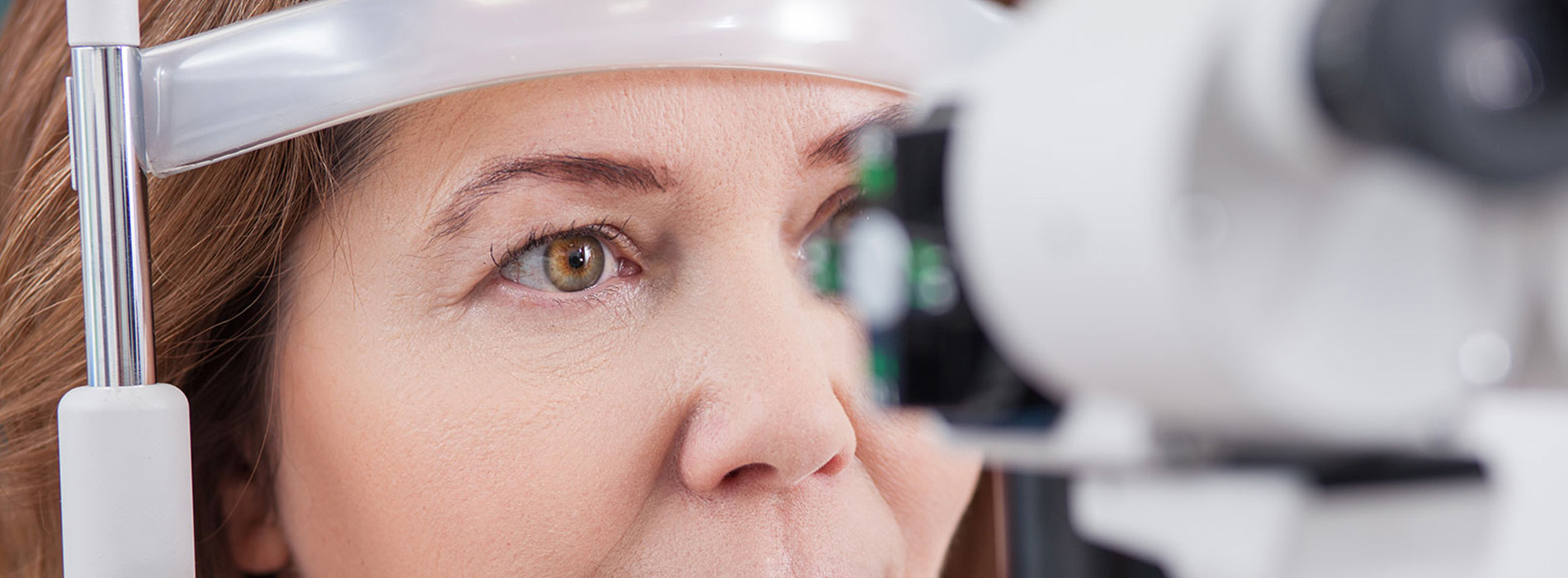 A woman undergoing an eye examination, with a focus on the eye machine and her gaze directed towards it.