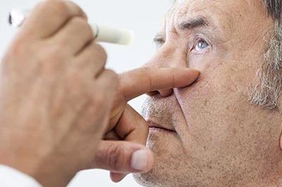 The image shows a man receiving an eye test, with a hand holding a device close to his eye.