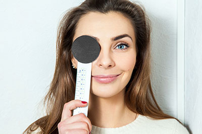 The image depicts a woman holding up a thermometer, with her face and the thermometer in focus against a blurred background.